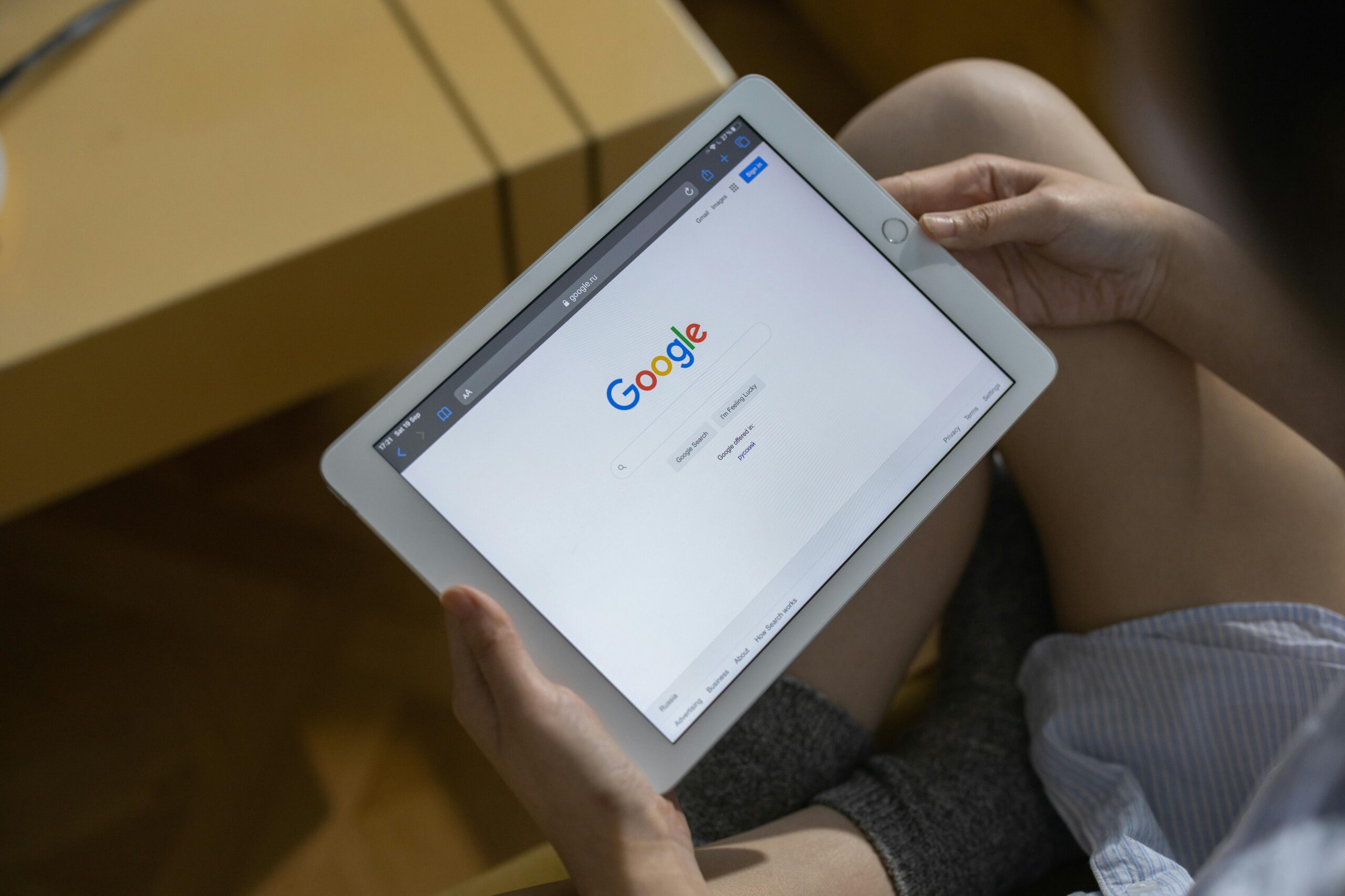 Close-up of hands holding a tablet showing the Google search page.